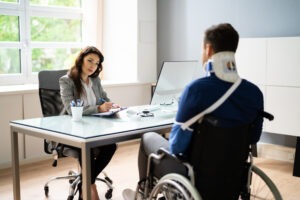 An experienced motorcycle accident lawyer in Berkey, discussing legal options with an injured client who is in a wheelchair and wearing an arm sling and a neck brace.